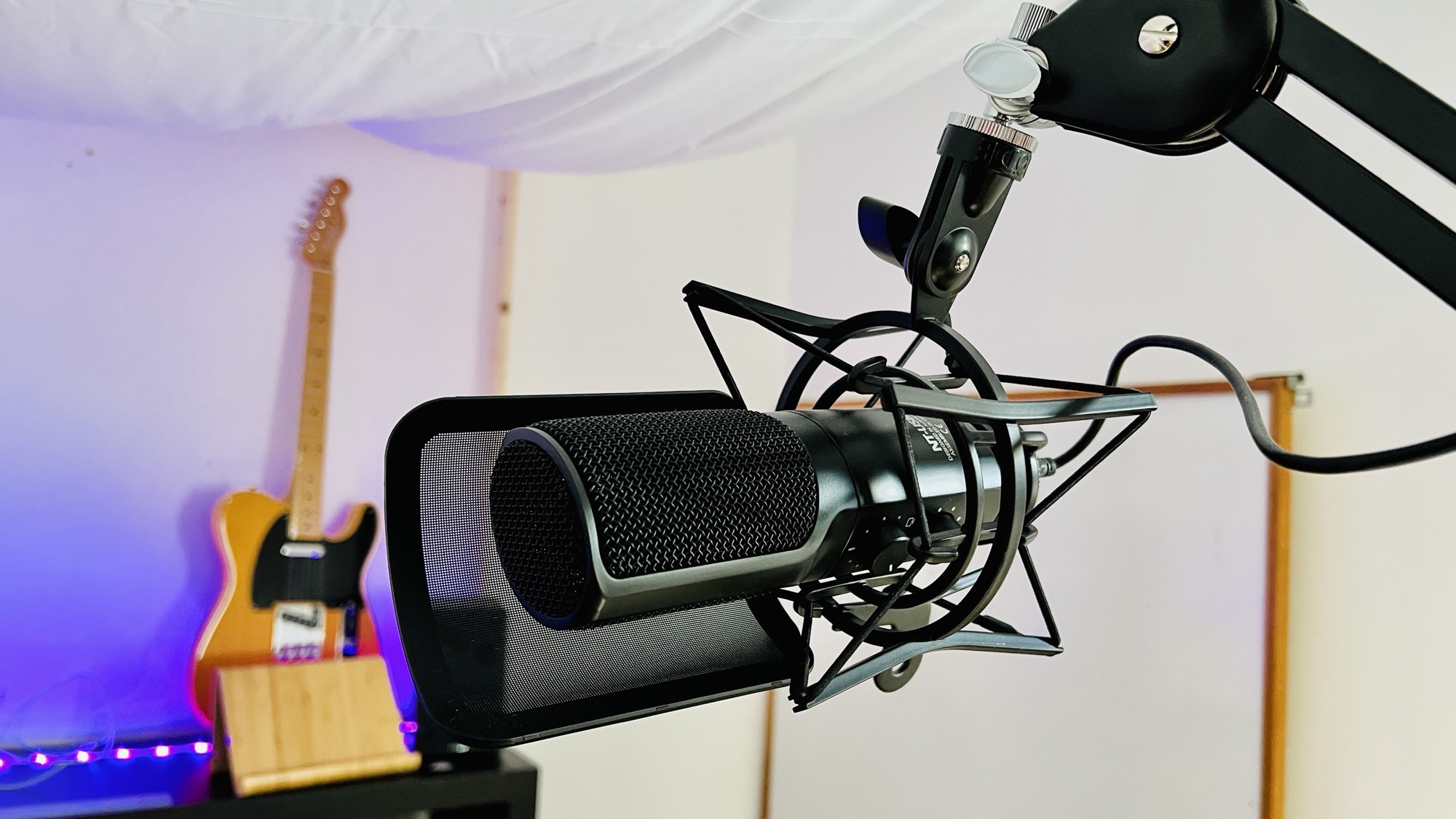 Røde NT-USB microphone mounted on boom arm with shock mount in a purple-lit studio setup